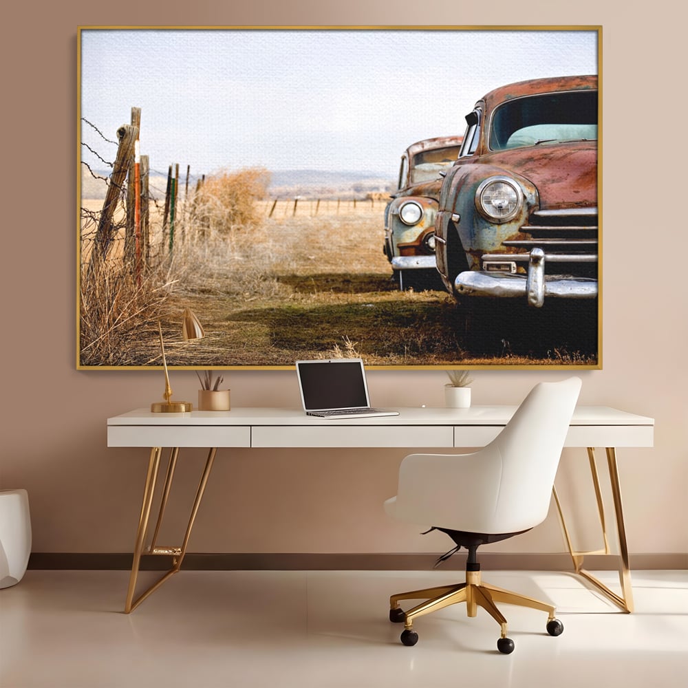 Tablou canvas cu doua masini ruginite pe un camp uscat, in rama de aluminiu auriu, pe perete intr-un birou